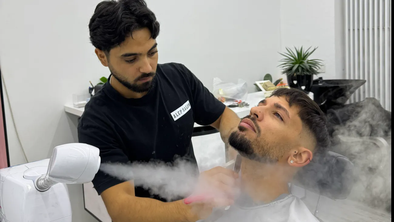 Ein Barbier im schwarzen Alep-Salon-Shirt pflegt den Bart eines Kunden mit warmem Dampf